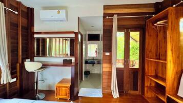 A wooden room with a bed, a desk, a mirror, a window, and a shower area.