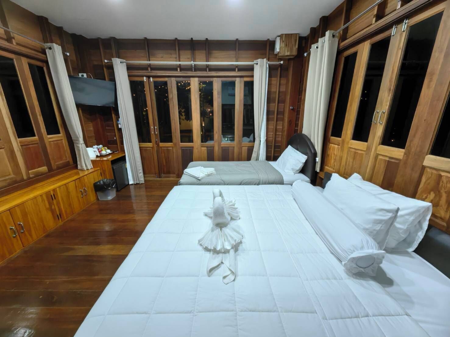 A hotel room with a large bed, wooden paneling, and a view through the windows.