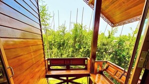 Een houten terras met een bank en een tafel, omgeven door weelderige begroeiing.
