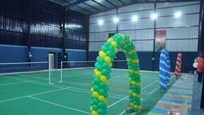 An indoor sports court with green flooring, a net, and a colorful arch made of balloons. - Selvam Residency (Thoothukudi)