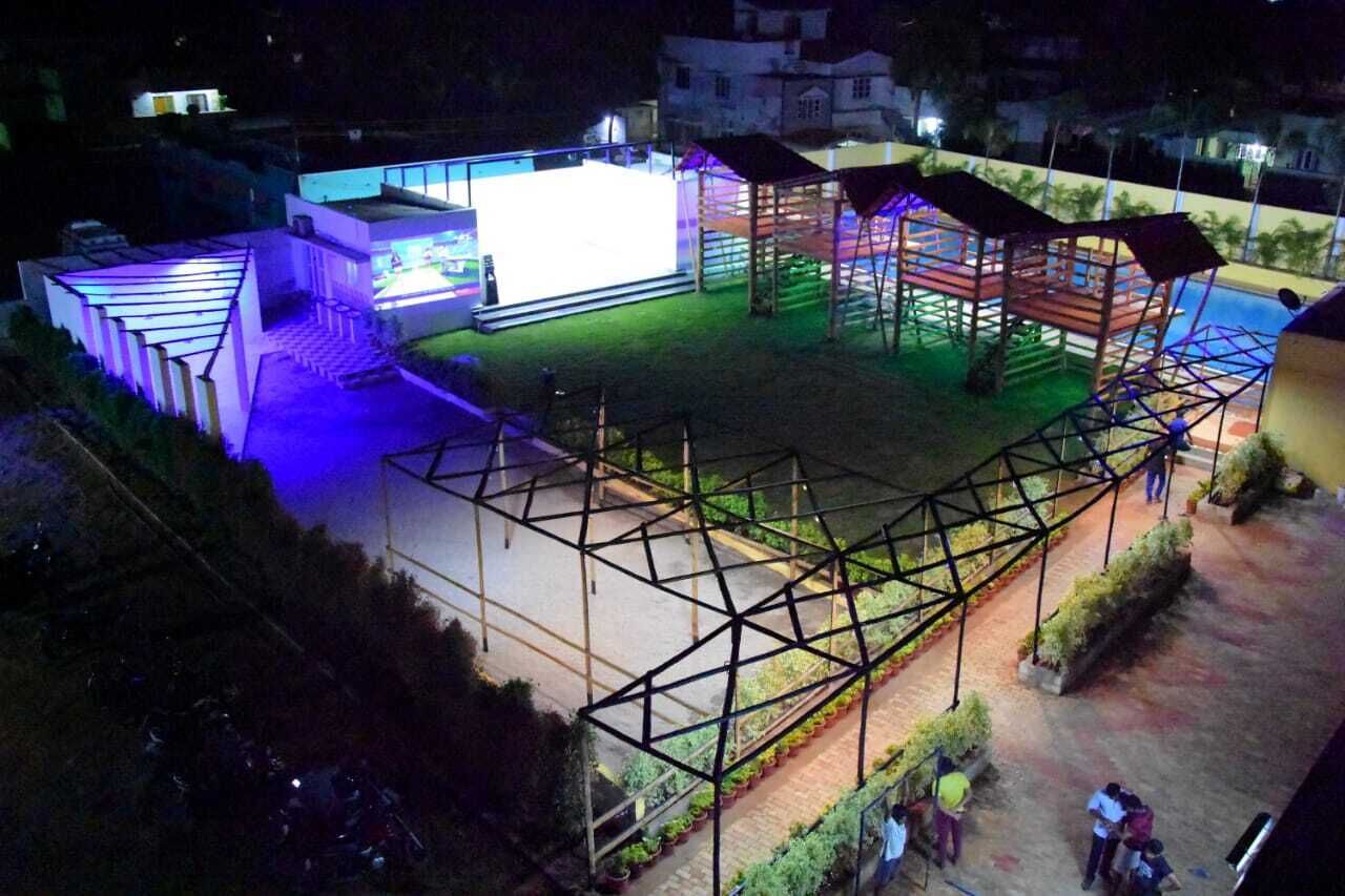 Un edificio moderno con una gran pantalla iluminada, un espacio exterior cubierto con asientos y una piscina.