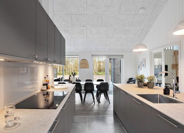 Une cuisine moderne avec des meubles de couleur sombre, un îlot central et un coin repas comprenant des chaises et une table.