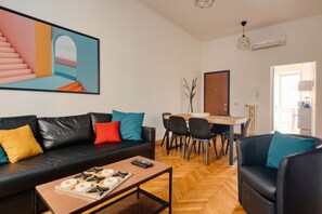A modern living room with a black leather sofa, a wooden coffee table, and a dining area with a wooden table and chairs.