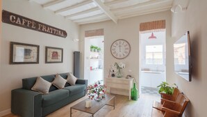 A living room with a green sofa, a coffee table with flowers, a clock, and a sign that reads "CAFFE FRATTINA". - THE BREAK - PIAZZA DI SPAGNA MAISON DELUXE TERRACE (Roma)