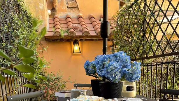 An outdoor patio with a table set for two, featuring a potted plant, a beverage container, and a menu. - THE BREAK - PIAZZA DI SPAGNA MAISON DELUXE TERRACE (Roma)