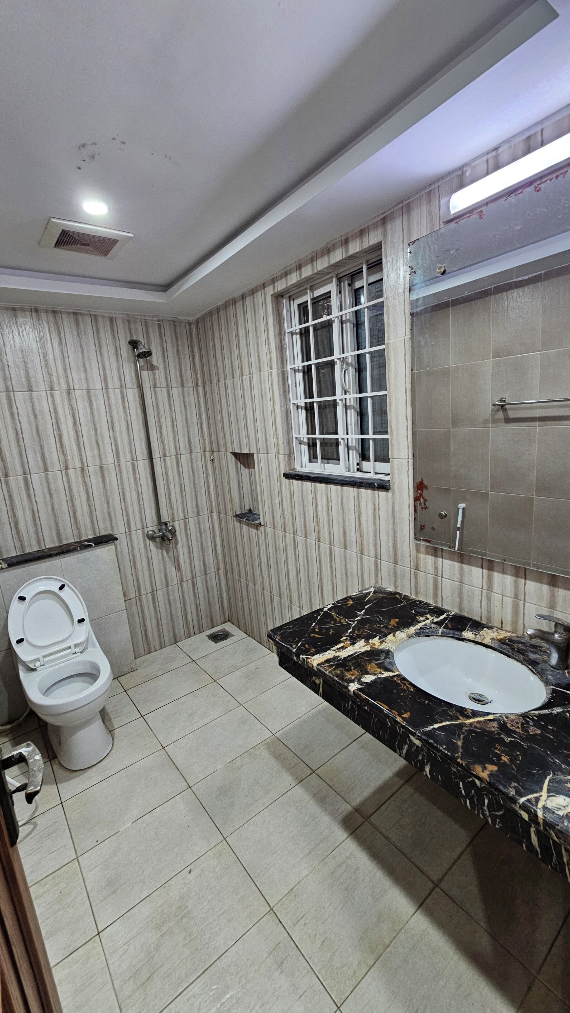 A bathroom with a toilet, sink, shower, and a window.