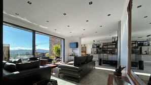 Een ruime woonkamer met een groot raam, een bank, een salontafel en een keuken op de achtergrond.