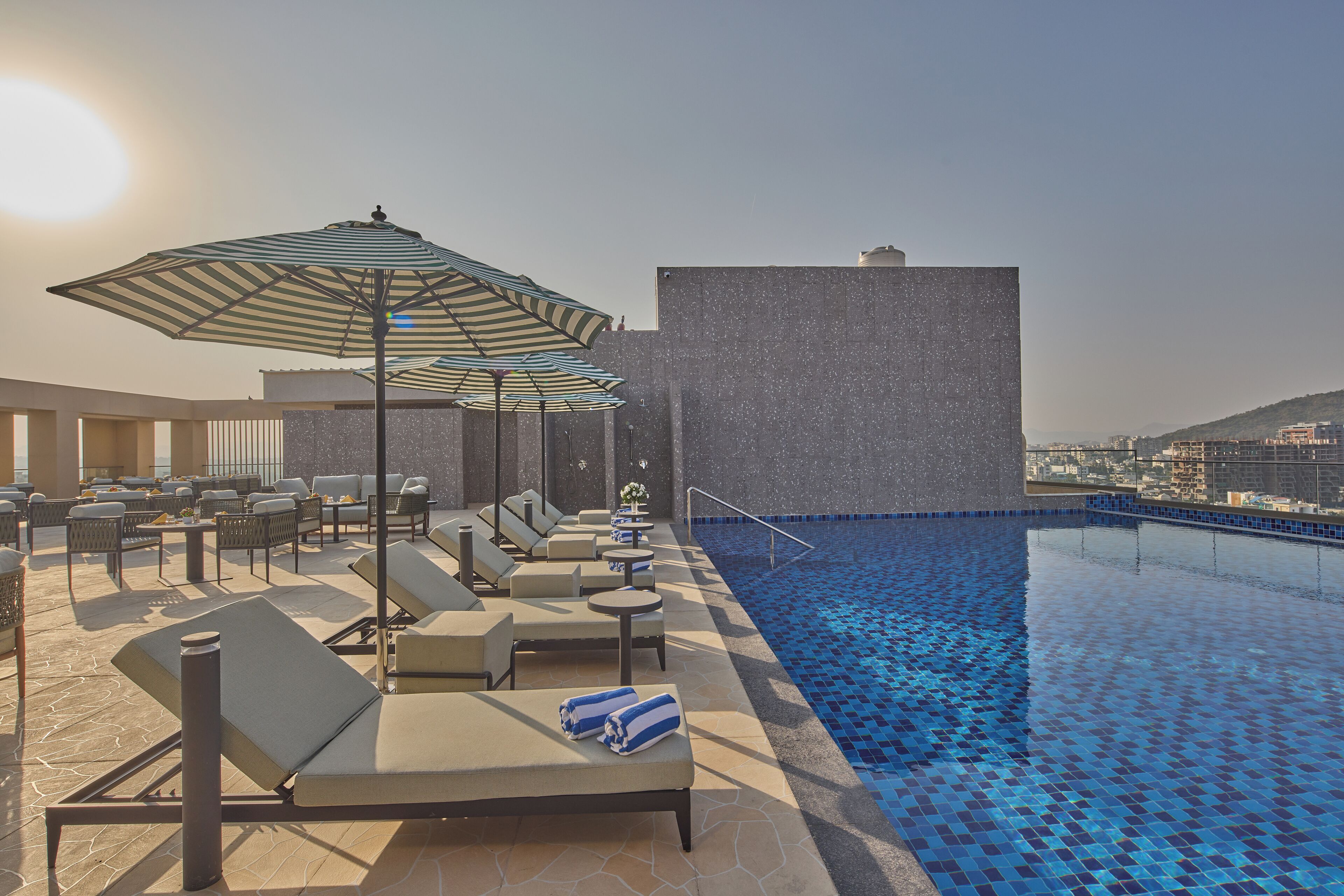A rooftop pool area with lounge chairs, umbrellas, and a view of the cityscape.