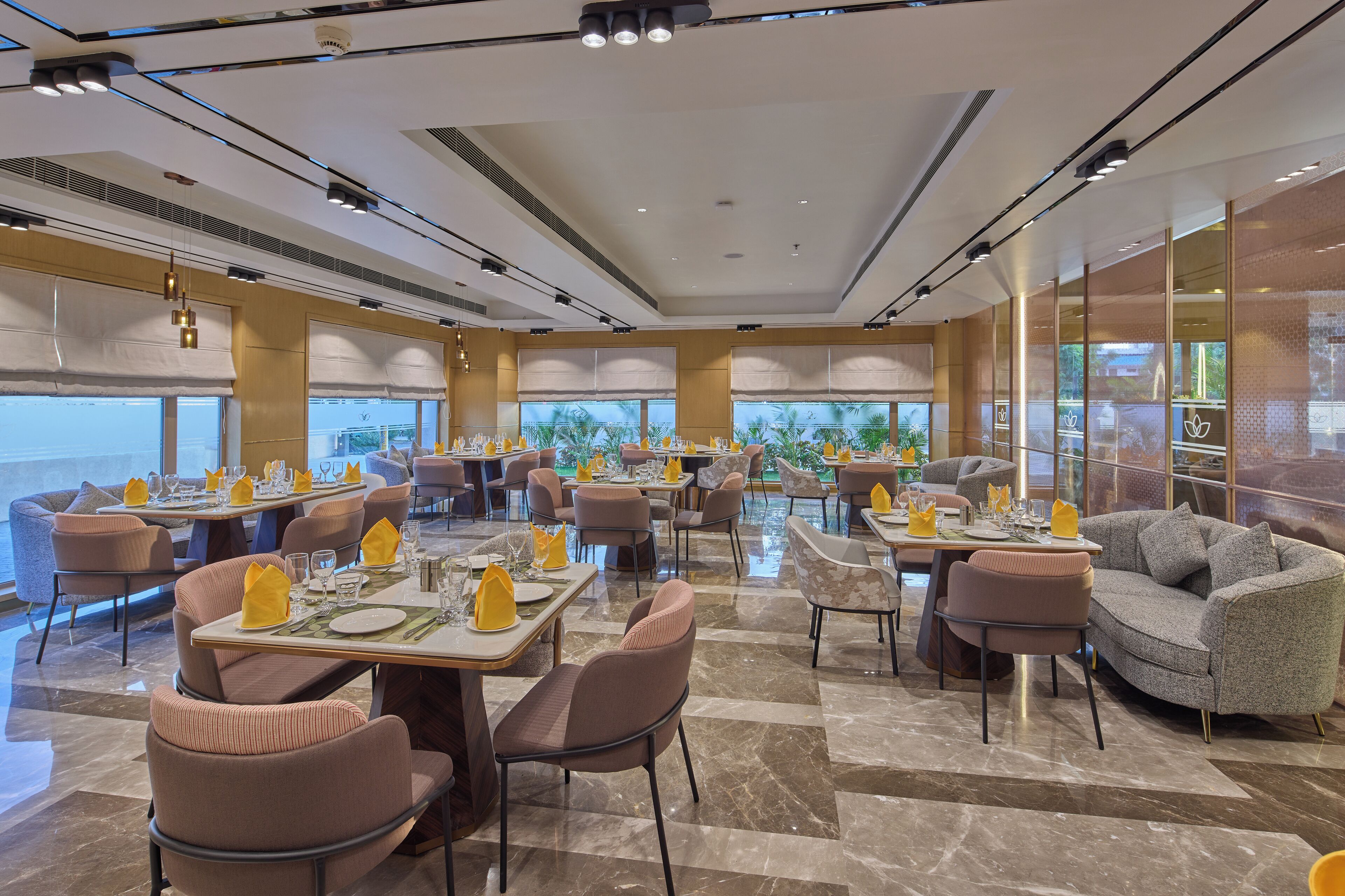A spacious dining area with multiple tables and chairs, large windows offering a view, and a modern ceiling design.