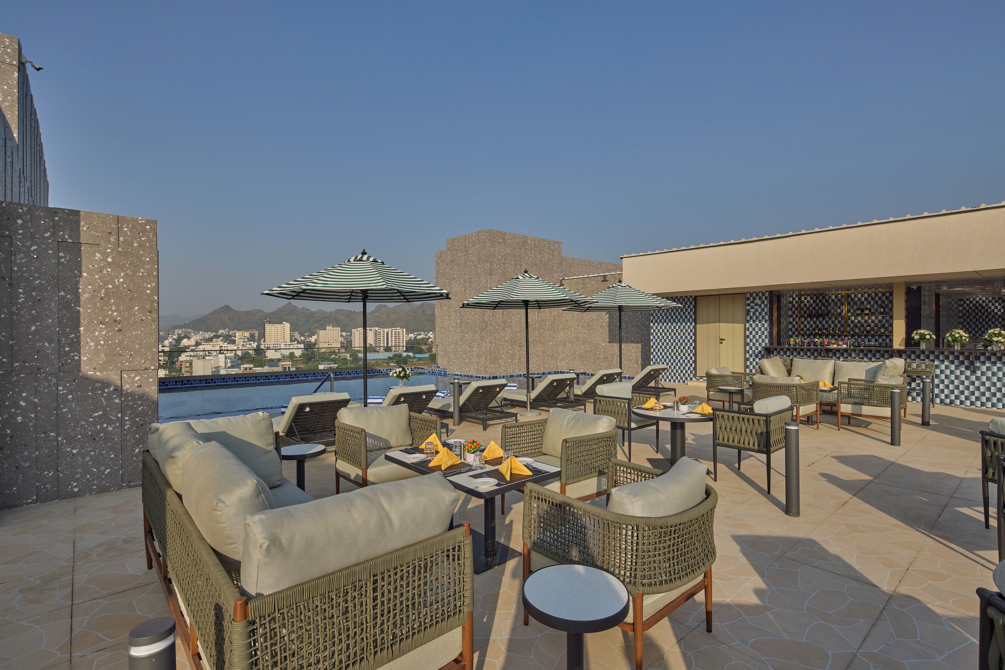 A rooftop terrace with wicker furniture, umbrellas, and a view of the cityscape.