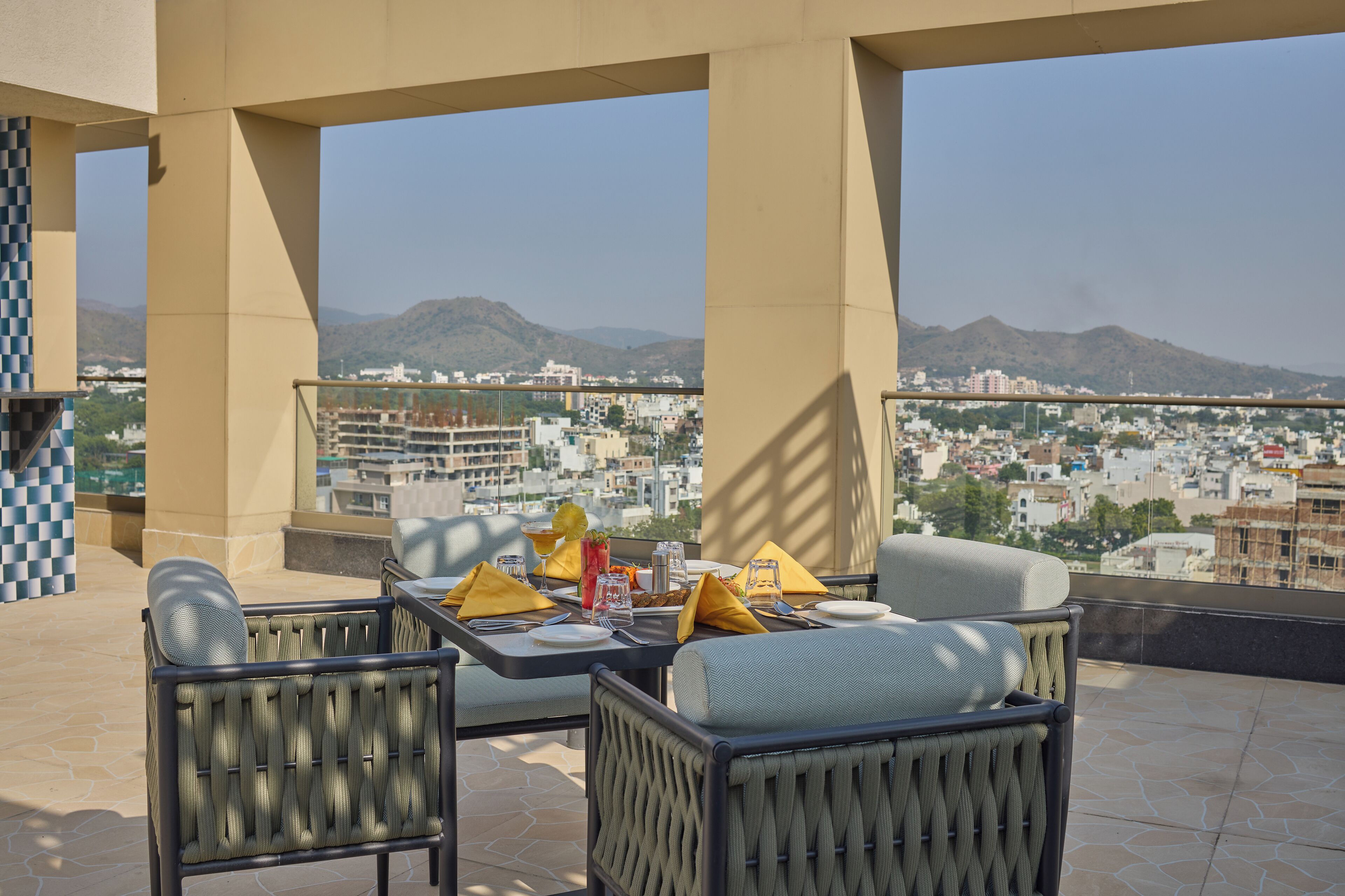 Eine Terrasse mit Korbmöbeln, einem gedeckten Esstisch und Blick auf die Stadt.