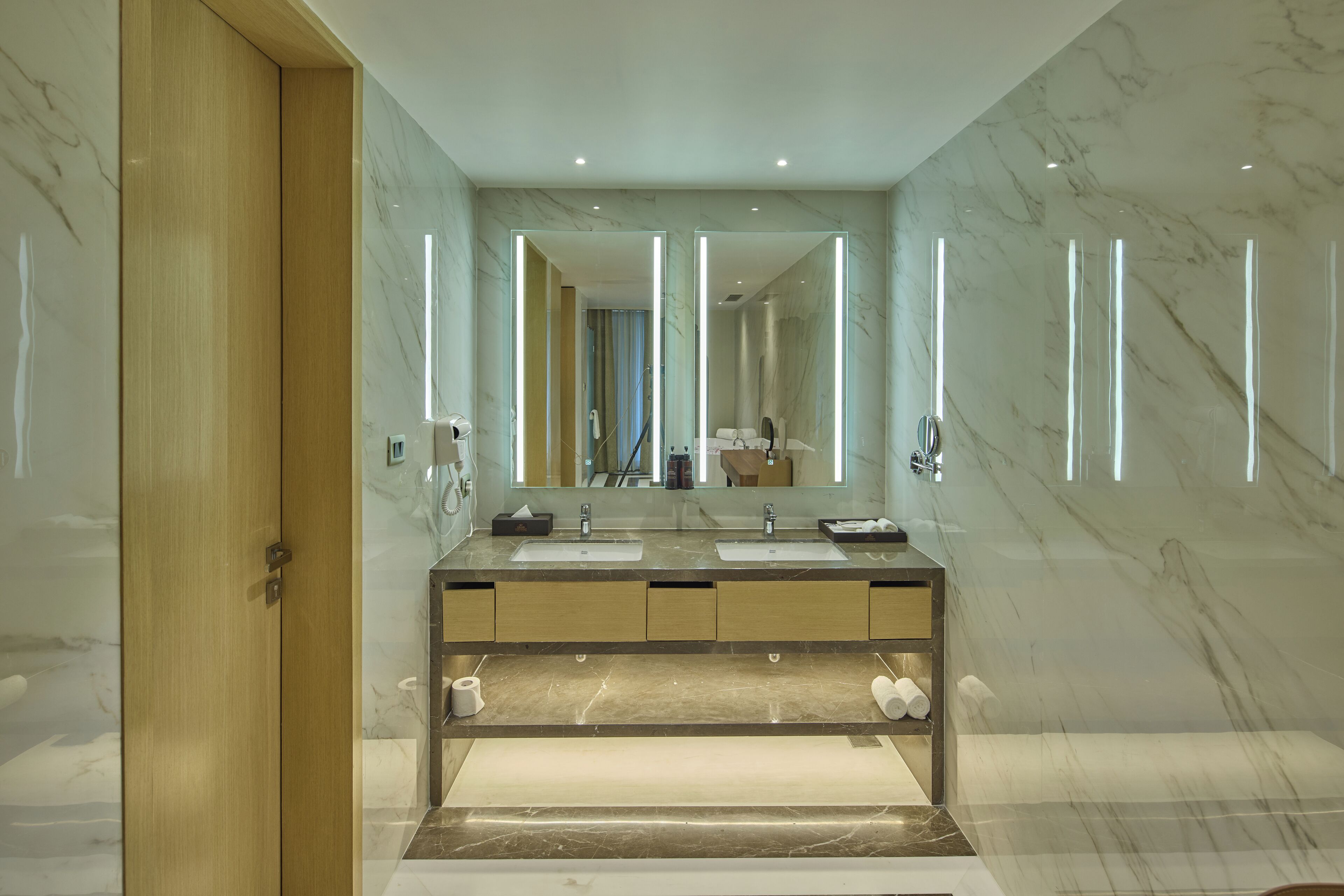 A modern bathroom with marble walls, a wooden door, and a double sink vanity.