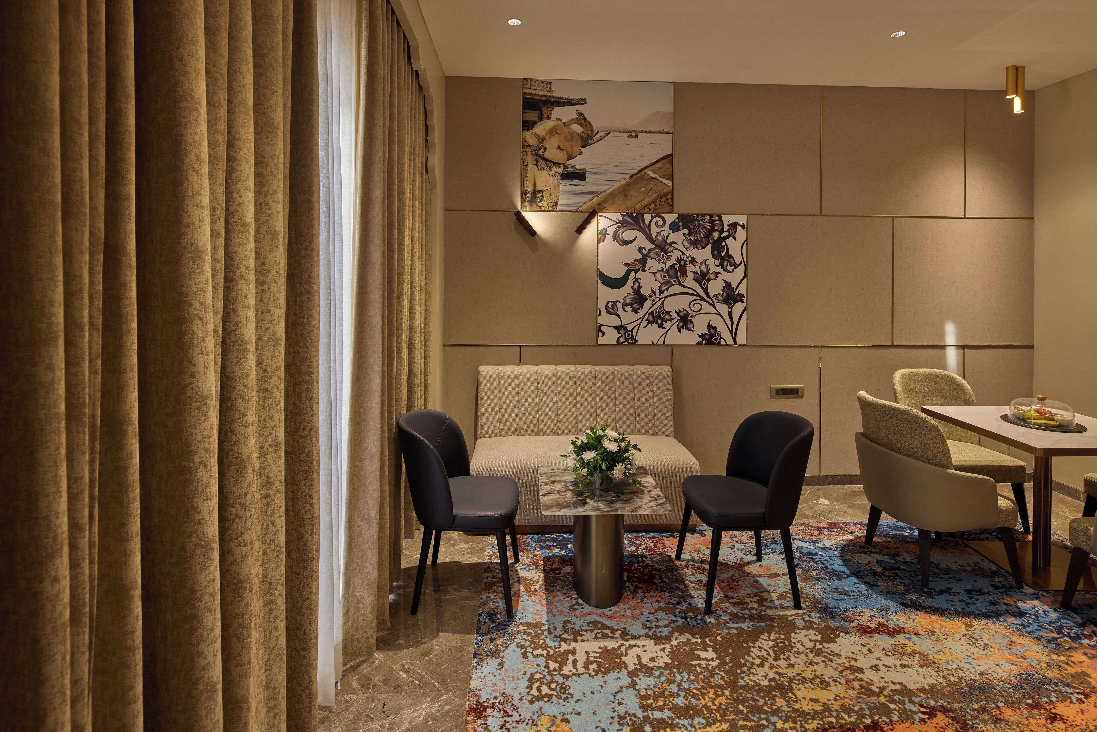 Une chambre d’hôtel moderne, dotée d’un canapé, de deux fauteuils, d’une petite table avec un vase et d’un tapis aux couleurs vives.
