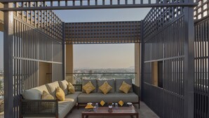 A balcony with a sofa, coffee table, and decorative pillows. - Grand Continent- A Luxury Collection Udaipur (Udaipur)