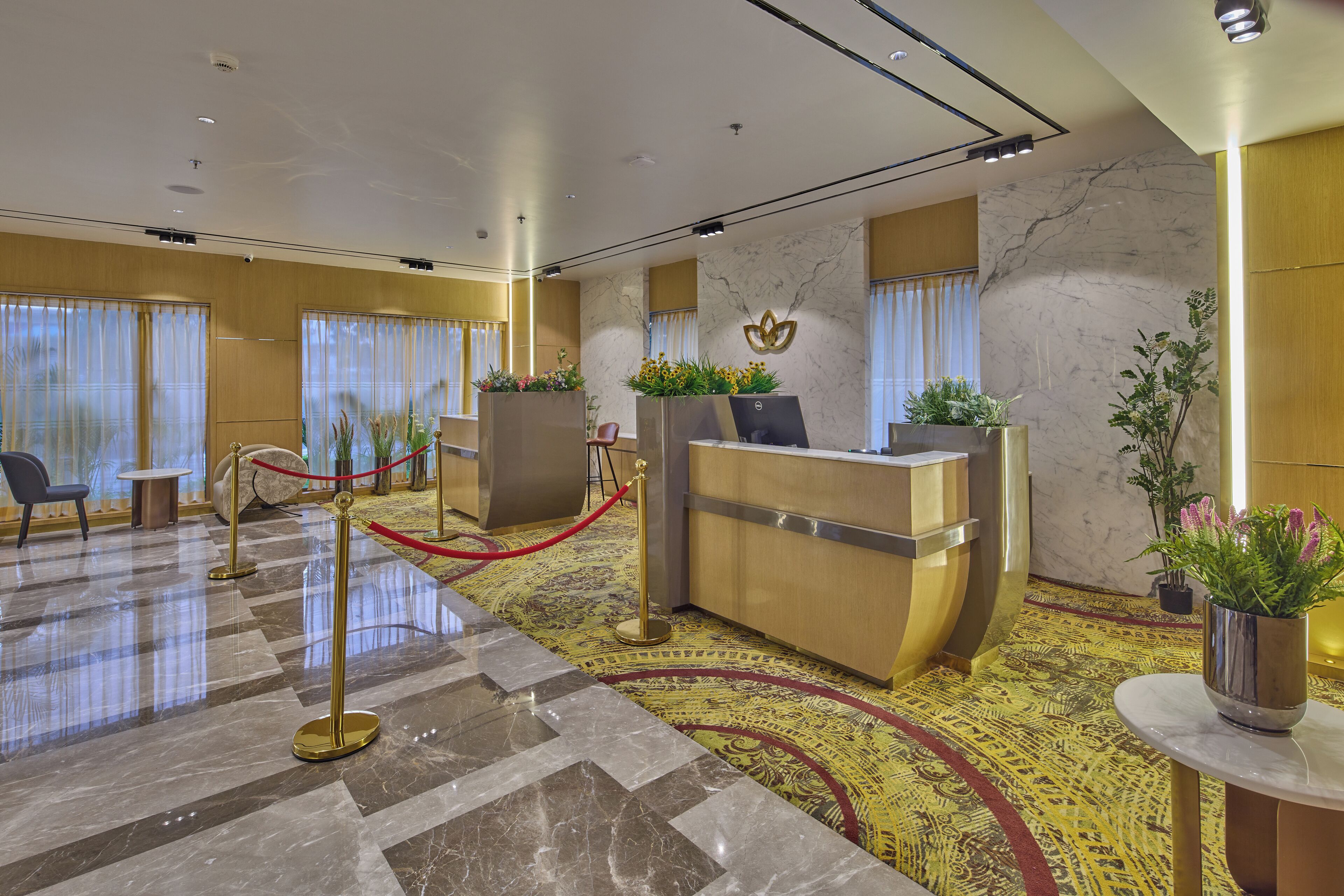 A hotel reception area with a marble floor, reception desk, and potted plants.