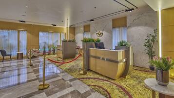A hotel reception area with a marble floor, reception desk, and potted plants.