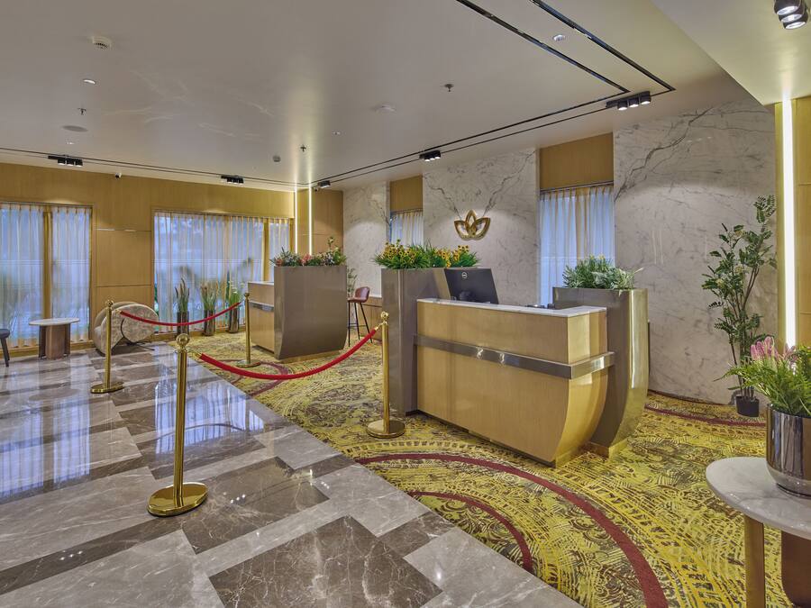 A hotel reception area with a marble floor, reception desk, and potted plants.