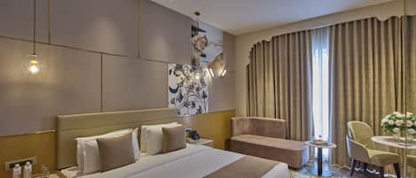 A hotel room with a large bed, a desk with a lamp, a chair, and a small table with a vase.