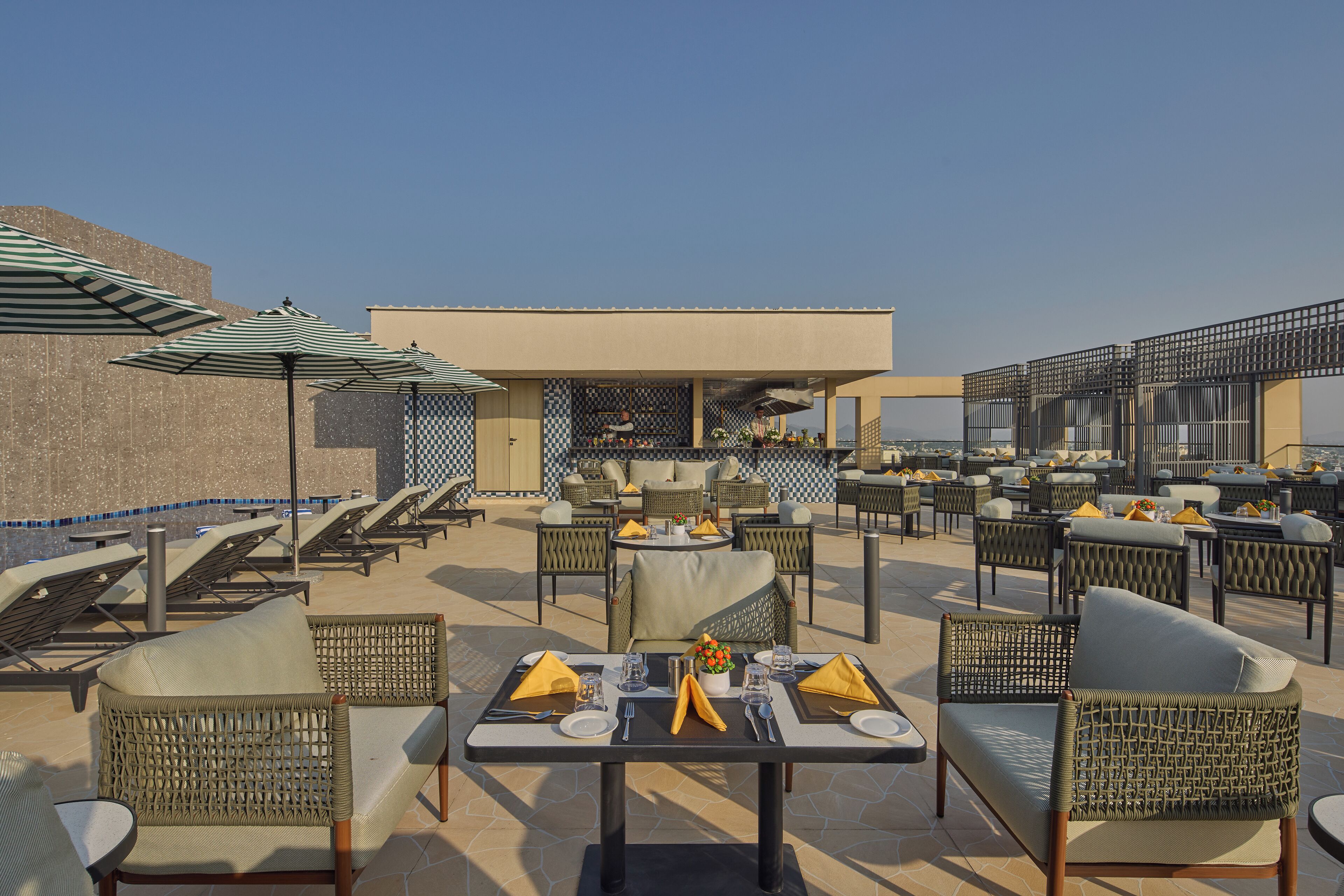 An outdoor patio with wicker furniture, tables set for dining, and umbrellas providing shade.