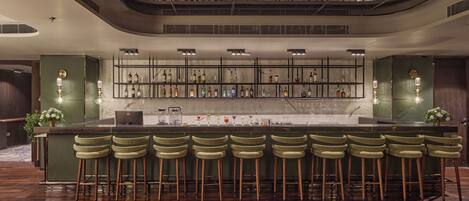 A bar area with a long counter, multiple stools, and a variety of bottles and glasses.