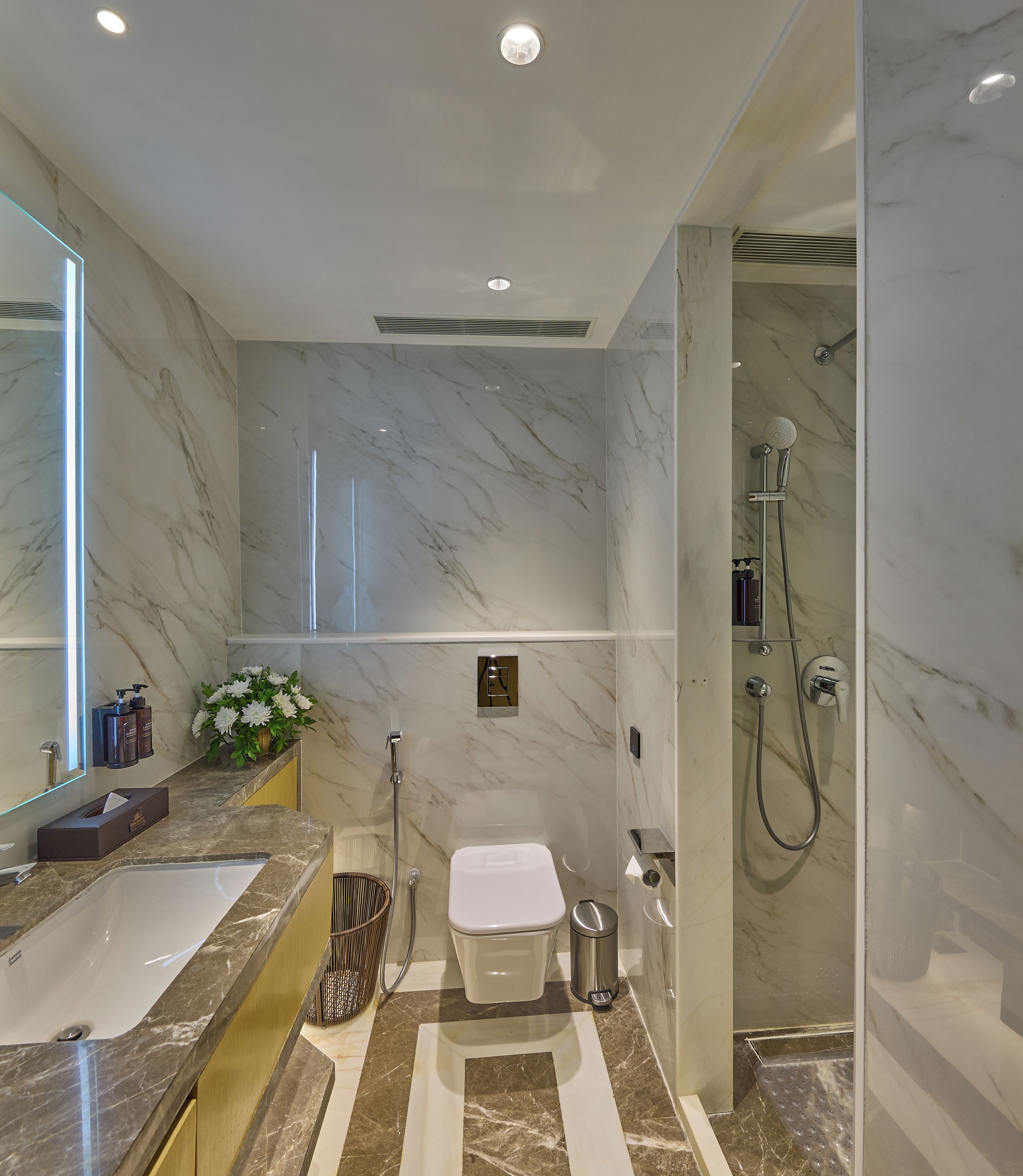 Une salle de bain moderne avec un sol en marbre, un grand miroir, une baignoire, des toilettes et une douche.