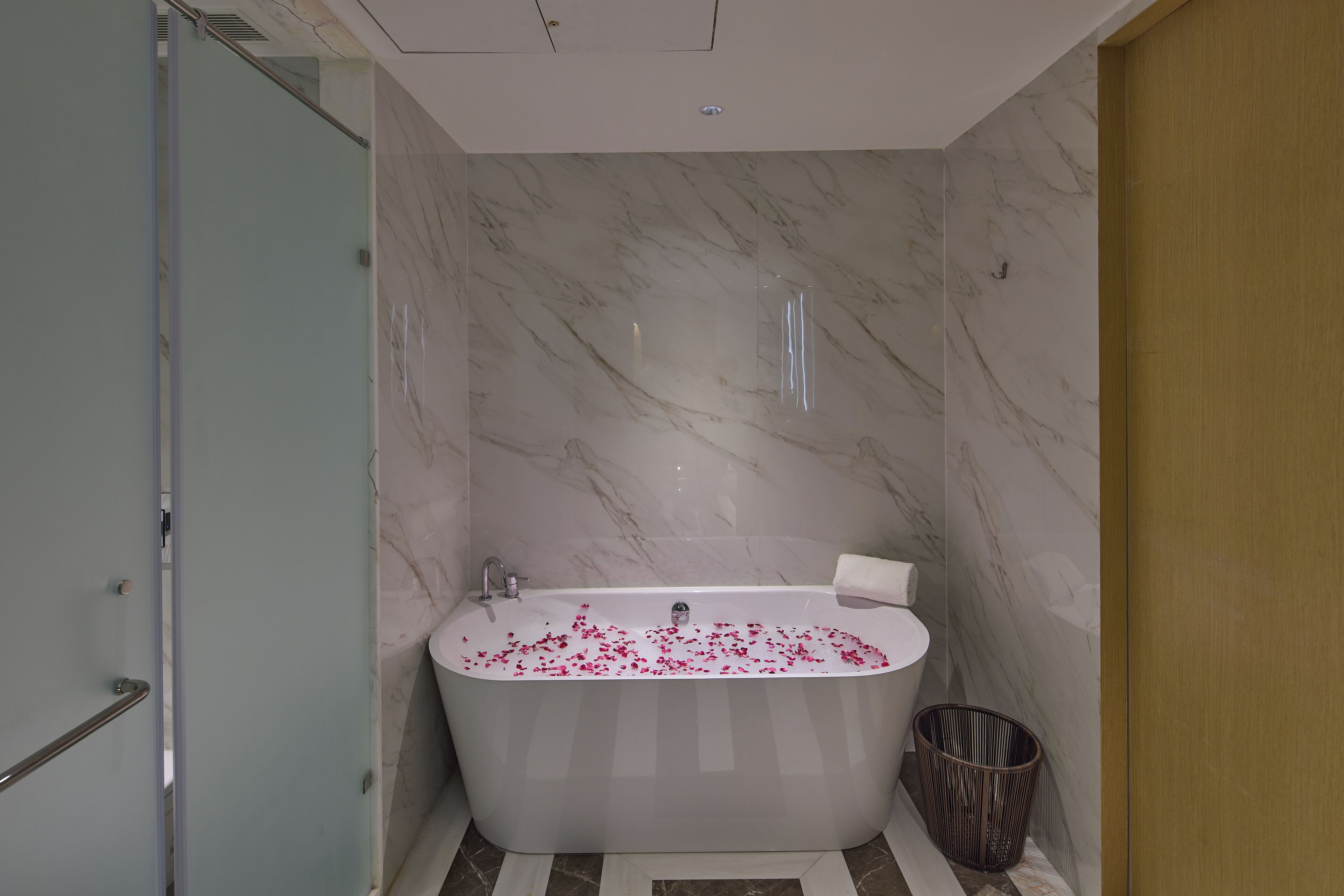 A modern bathroom with a marble wall, a freestanding bathtub, and a shower area.