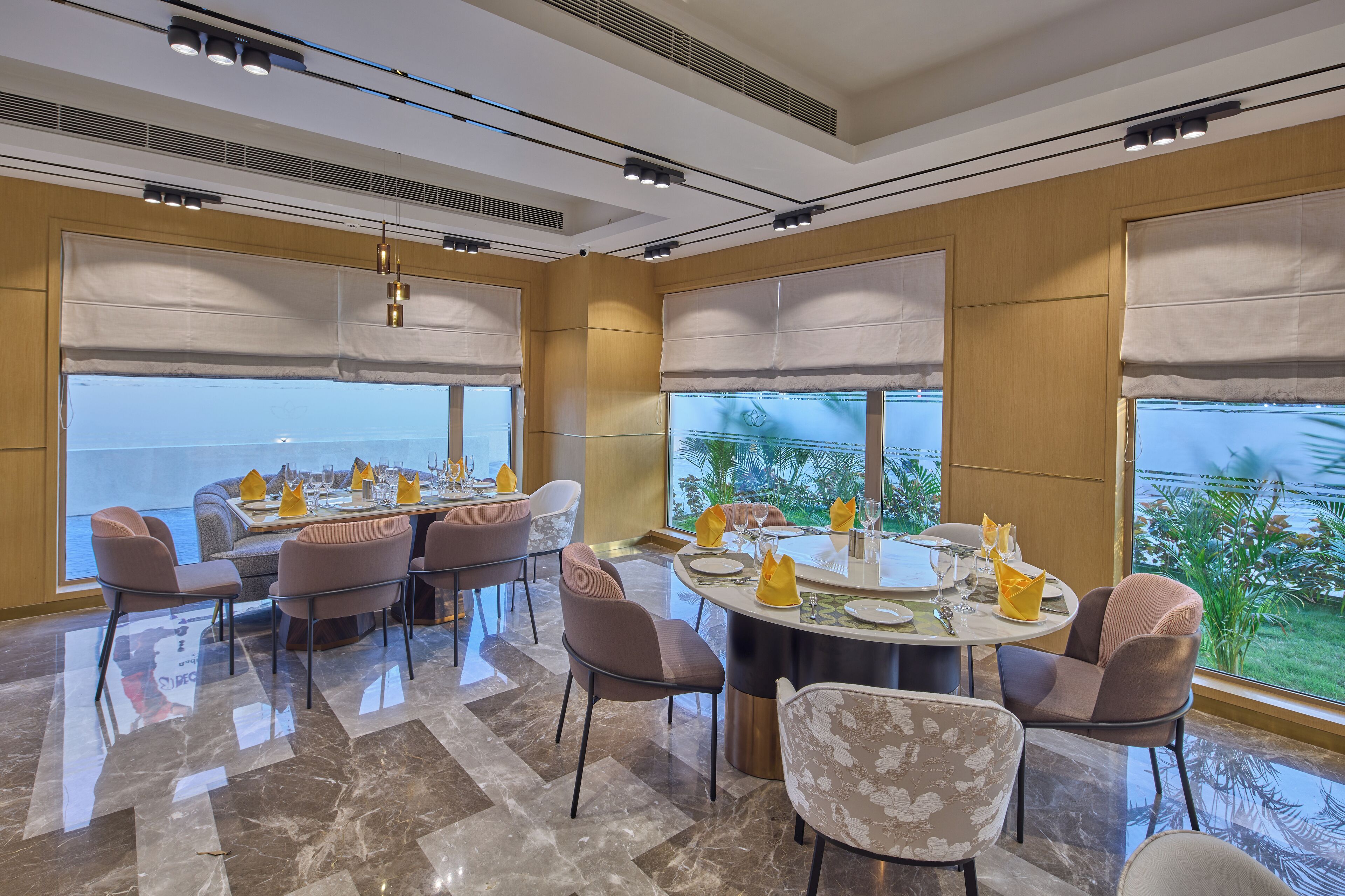A modern dining area with a large round table, multiple chairs, and a view of the ocean through large windows.