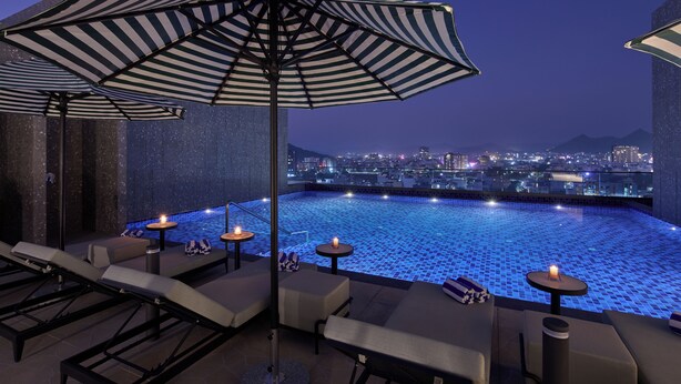 A rooftop infinity pool with lounge chairs and umbrellas, overlooking a cityscape at night. - Grand Continent- A Luxury Collection Udaipur (Udaipur)