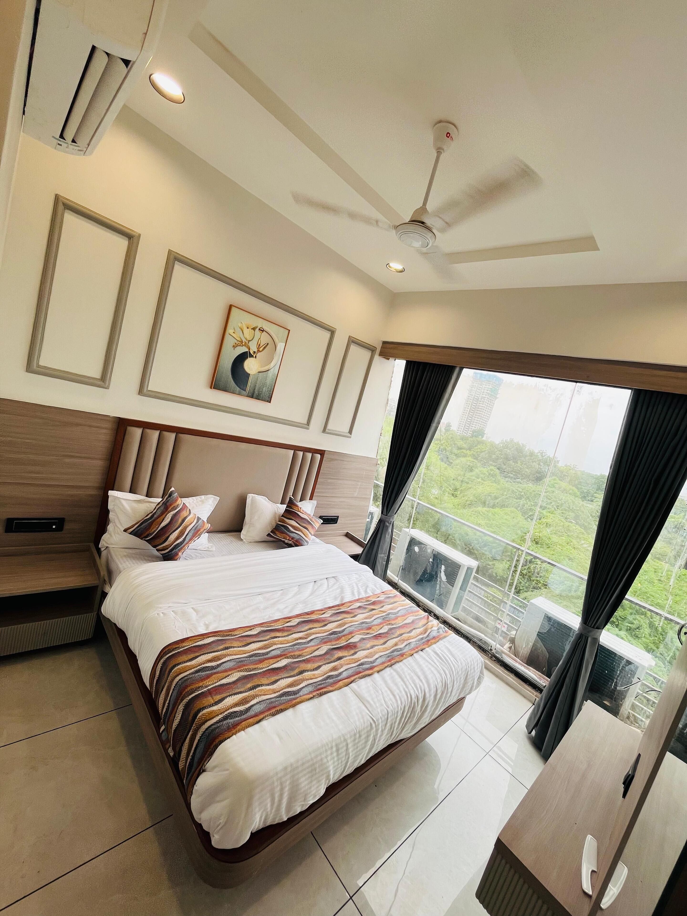 A modern bedroom with a large bed, a ceiling fan, and a view of greenery through the window.