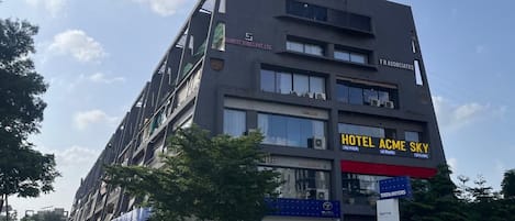 A multi-story building with a sign for "Hotel Acme Sky" and a Tata Motors dealership on the ground floor.
