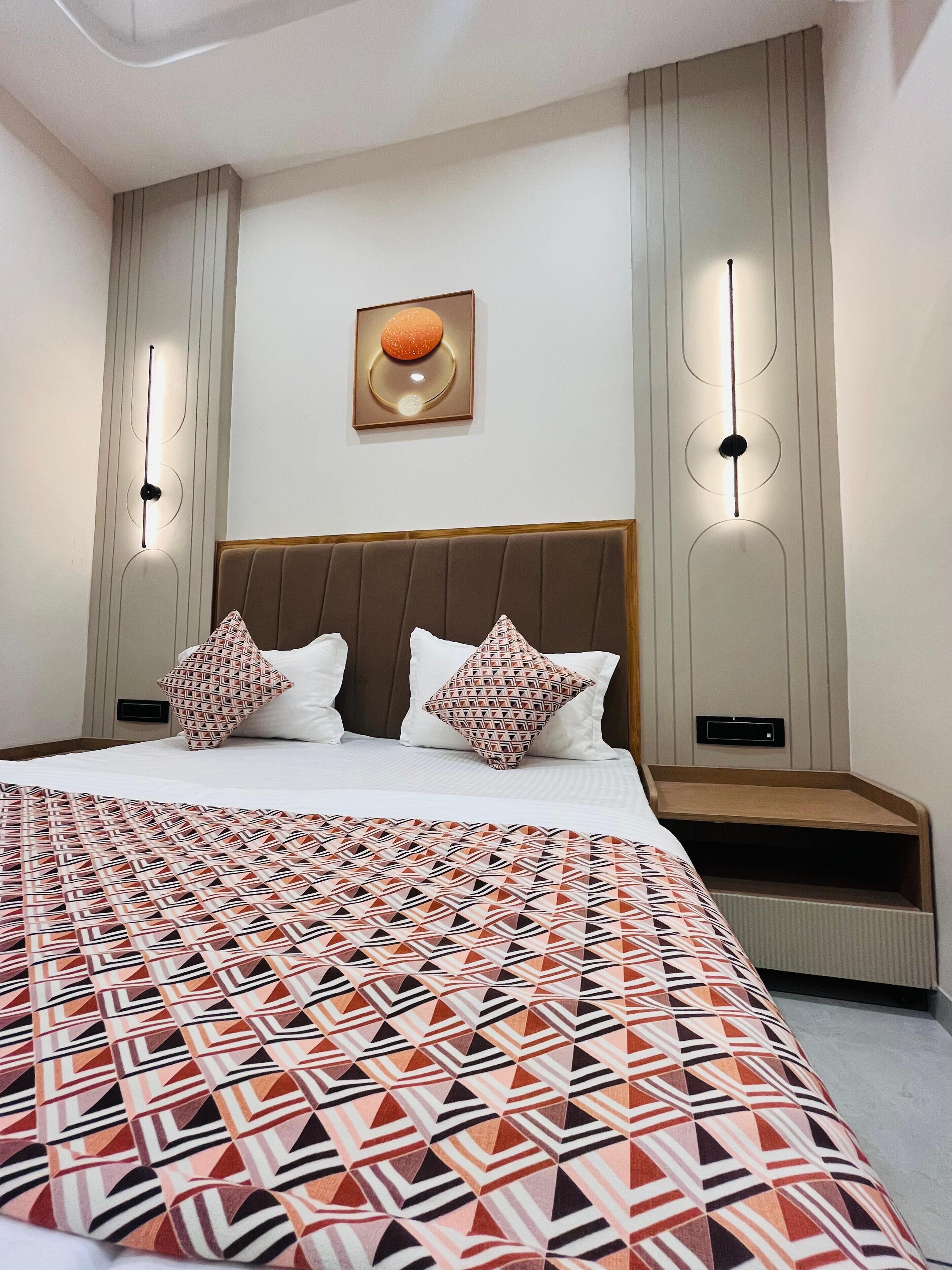 Une chambre d’hôtel moderne avec un grand lit, une tête de lit, un tableau accroché au mur et deux appliques murales.
