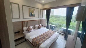 A modern hotel room with a large bed, a ceiling fan, and a view of greenery outside.