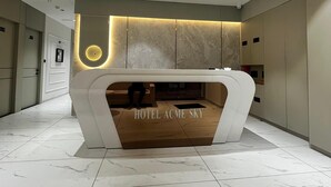 A modern hotel reception area with a marble floor, a central desk with the hotel name, and a circular light fixture above.