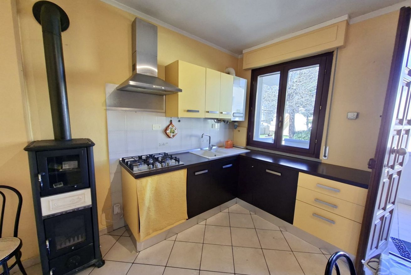 Une cuisine compacte équipée d’une cuisinière à gaz, d’une hotte noire et d’une fenêtre laissant entrer la lumière naturelle.