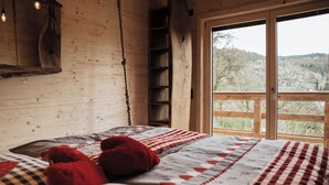 A wooden cabin bedroom with a large window, a ladder, and a bed with patterned bedding. - Romantic Chalet Vogelnest | Peace & Comfort in Nature of Franconian Switzerland (Vorra)