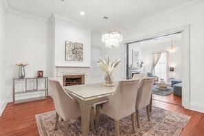 A dining room with a wooden table, four chairs, a fireplace, and a chandelier.