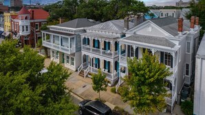Une rangée de maisons de style victorien, à plusieurs étages, dotées de larges porches à l’avant, et une rue étroite bordée d’arbres.