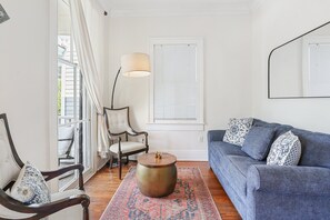 A living room with a blue sofa, patterned pillows, a round coffee table, a floor lamp, a chair, and a patterned rug. - Stay on Broughton, Downtown Savannah, Sleeps 10 (Savannah)