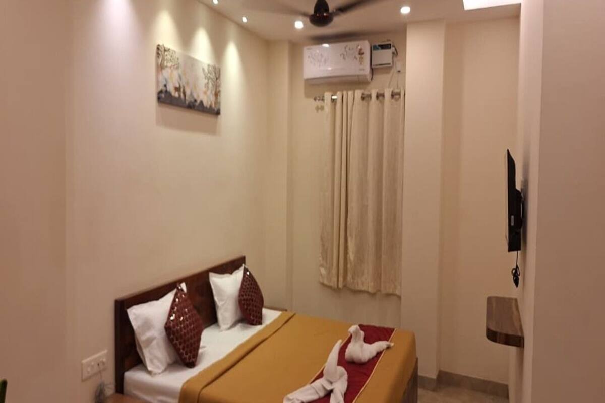 A hotel room with a bed, a nightstand, an air conditioning unit, a ceiling fan, a painting on the wall, and a curtain.