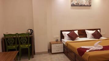 Habitación de hotel con una cama, dos sillas verdes, una mesita, una mesilla de noche y un cuadro en la pared.