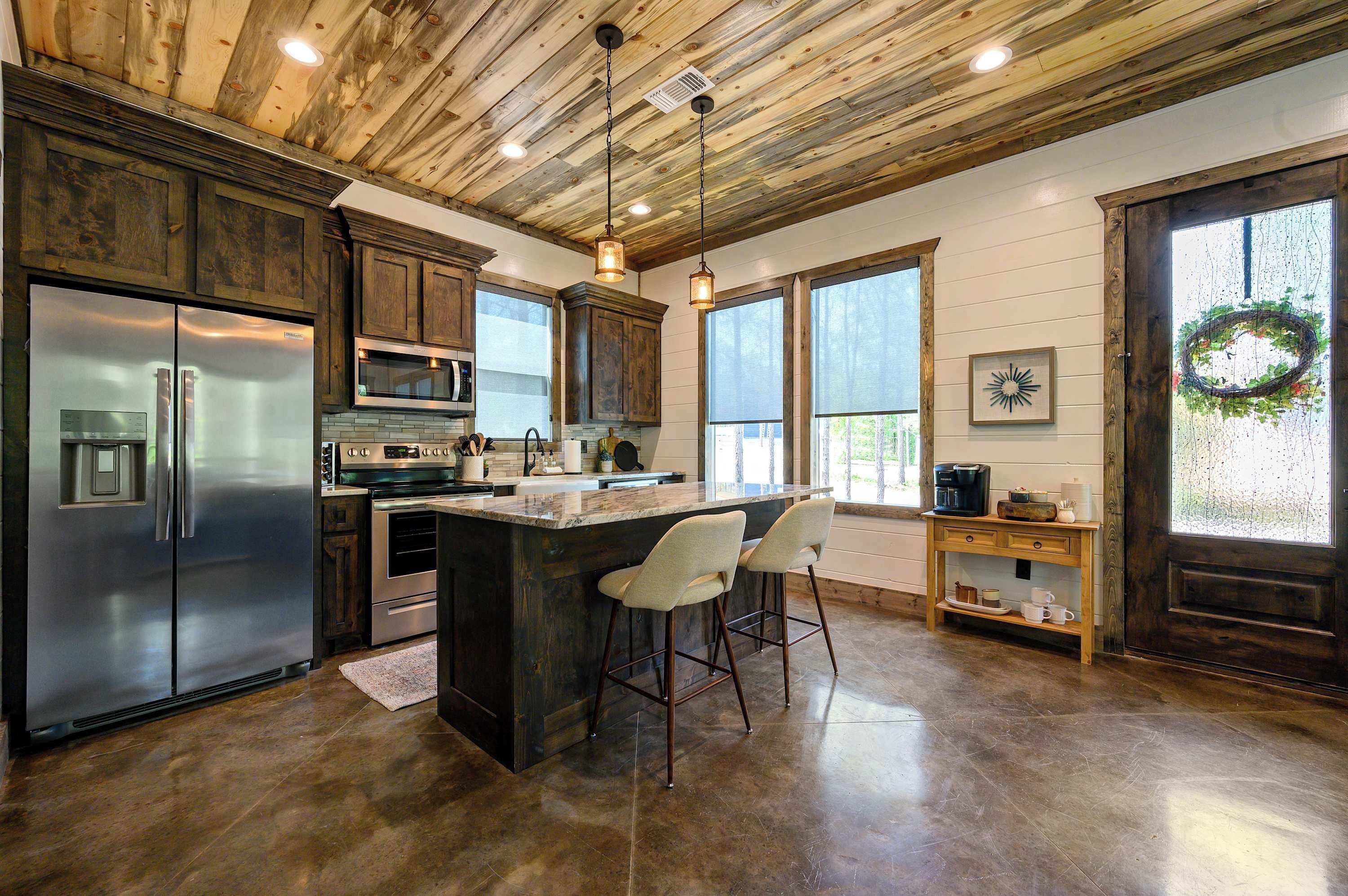 A kitchen with a large island, bar stools, stainless steel appliances, and a wooden ceiling.