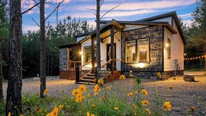A cabin with a stone exterior, wooden deck, and large windows. - New! At Ease Romantic Honeymoon Cabin Hot Tub (Broken Bow)