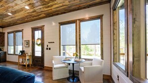 A room with a wooden ceiling, white walls, a round table with chairs, and large windows. - New! At Ease Romantic Honeymoon Cabin Hot Tub (Broken Bow)
