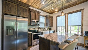 A kitchen with a stainless steel refrigerator, built-in oven, and a large island with bar stools. - New! At Ease Romantic Honeymoon Cabin Hot Tub (Broken Bow)