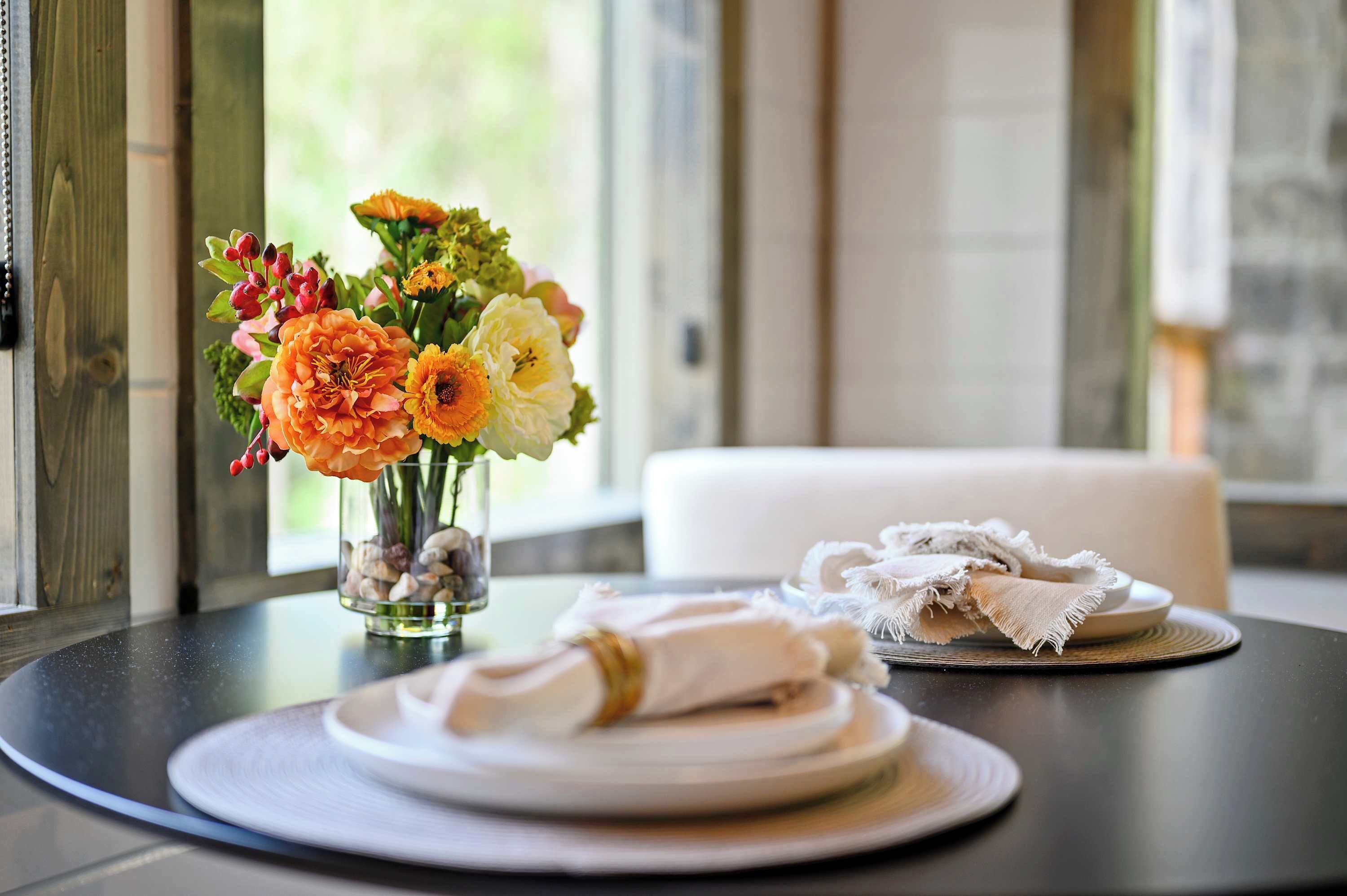 A dining table with a vase of flowers, a folded napkin, and a plate.