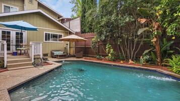 A backyard with a swimming pool, a covered patio area, and a wooden fence.