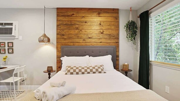 Een netjes ingerichte slaapkamer met een houten hoofdbord, een nachtkastje, een hangplant en een raam met gordijnen.