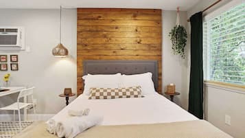 A neatly arranged bedroom with a wooden headboard, a bedside table, a hanging plant, and a window with curtains.