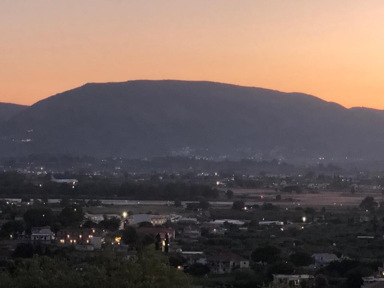 A cityscape at dusk with a prominent hill in the background.