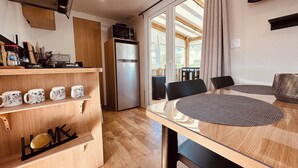 A modern kitchen with a built-in refrigerator, wooden shelves, and a dining area with a round table and chairs. - Mobile home - 2 bedrooms - air conditioning - Enclosed terrace - Locsweethome (Les Mathes)